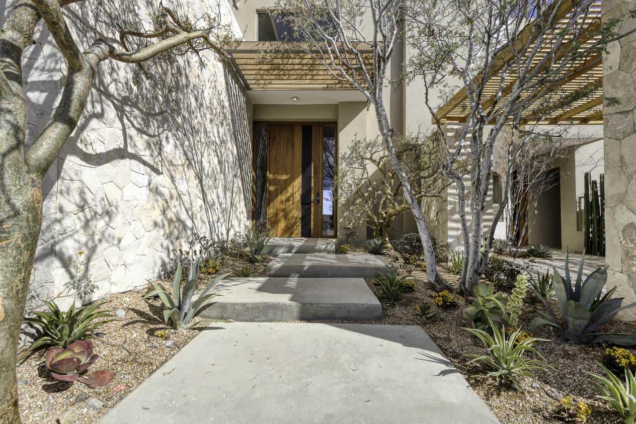 Modern Home Entrance With Desert Landscaping, Trees, And Natural Stone Accents At Club Campestre, Offering Golf Course And Ocean Views.