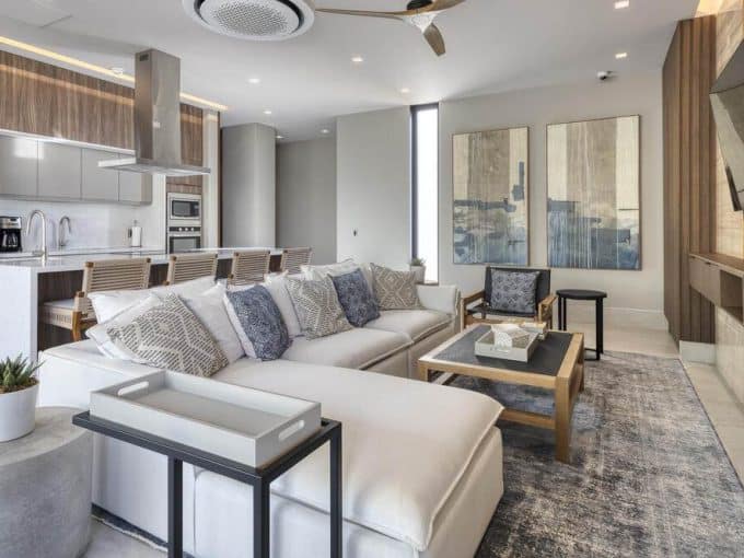 Modern Living Room With Ocean View And Golf Course Backdrop At Club Campestre Real Estate, Featuring Stylish Decor, A Flat-Screen Tv, And Open-Concept Kitchen.