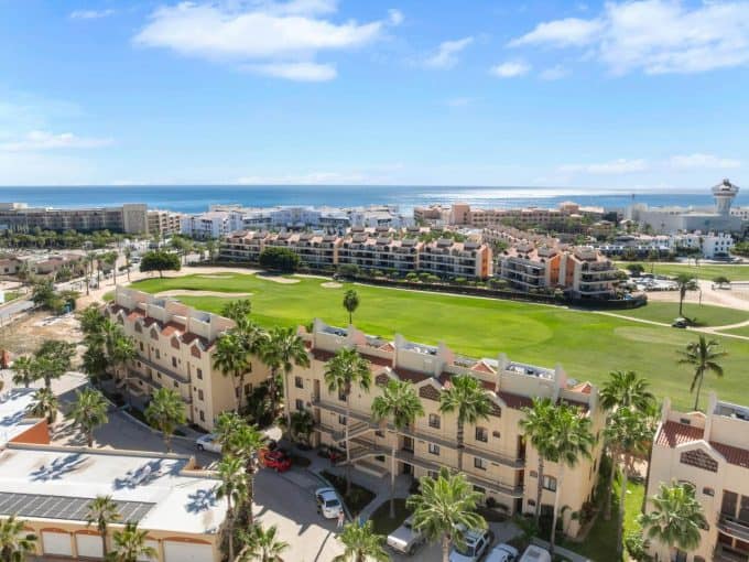Luxurious Golf Course And Ocean View From Vibrant Residential Community At Club Campestre, Featuring Scenic Green Fairways, Modern Buildings, Palm Trees, And Distant Shoreline.