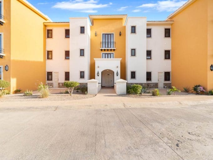 Modern Apartment In A Golf Community With Ocean Views At Club Campestre, Featuring Vibrant Yellow And White Exterior, Lush Landscaping, And A Scenic Coastal Backdrop.