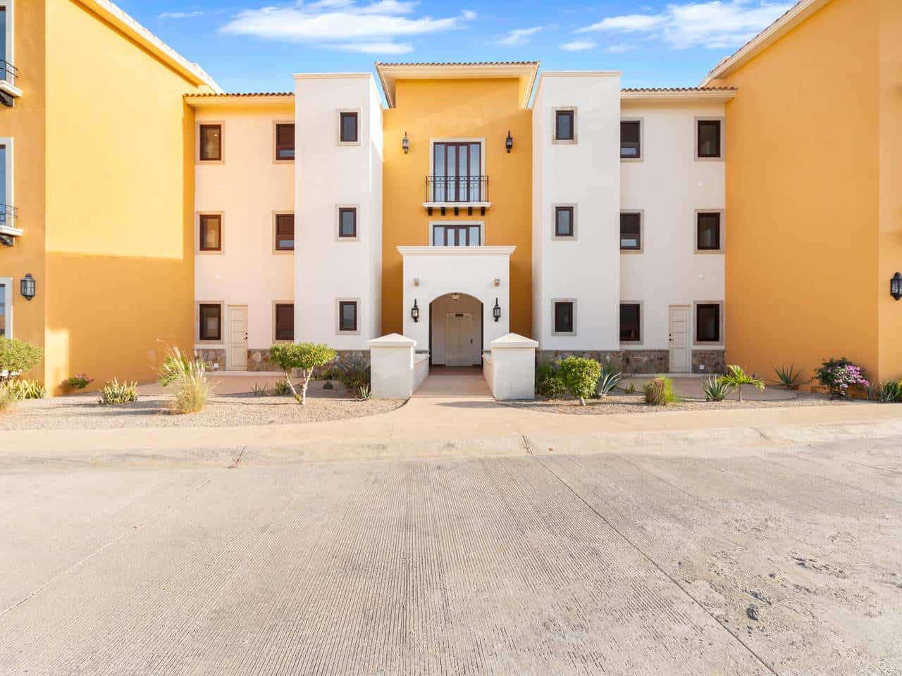 Modern Apartment In A Golf Community With Ocean Views At Club Campestre, Featuring Vibrant Yellow And White Exterior, Lush Landscaping, And A Scenic Coastal Backdrop.