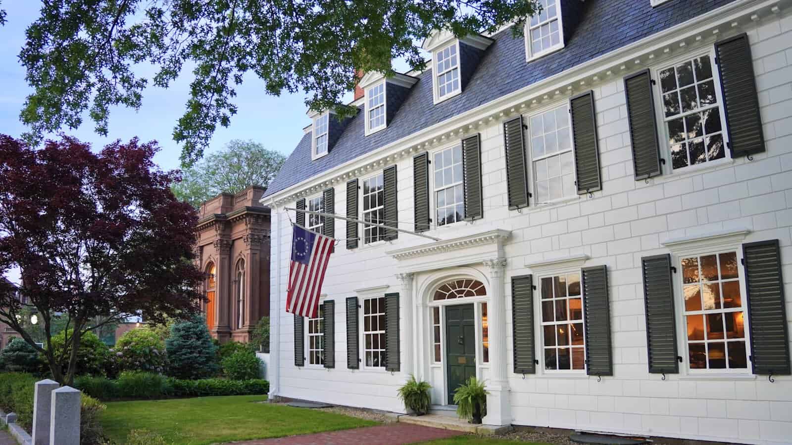 White New England colonial home with dark shutters showing classic siding and trim color contrast