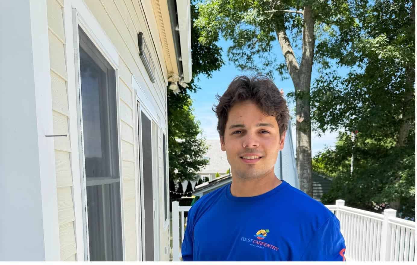 Coast Carpentry Home Group crew member in a branded shirt beside clapboard siding at a white-railed Cape Cod deck