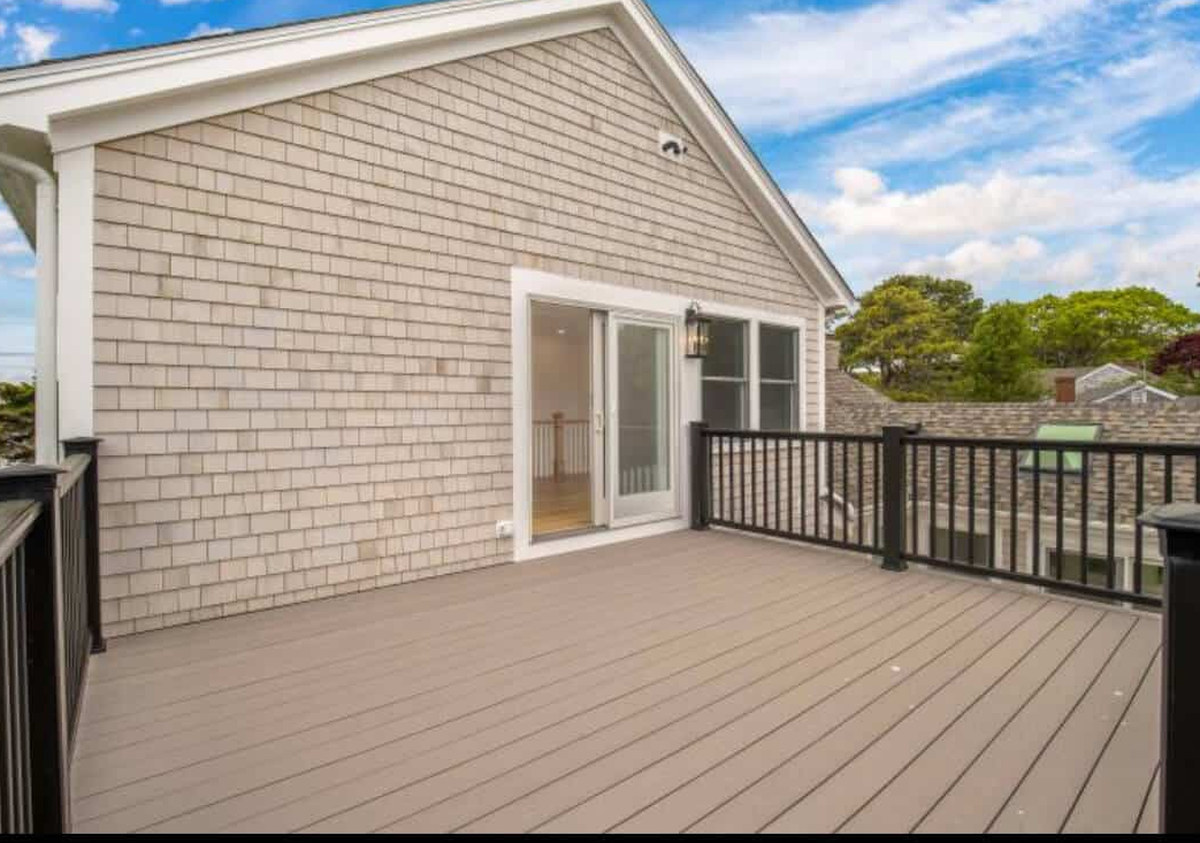 New white cedar shingle siding on the gable end of a Coast Carpentry remodel in Hyannis, MA, with a new slider and deck