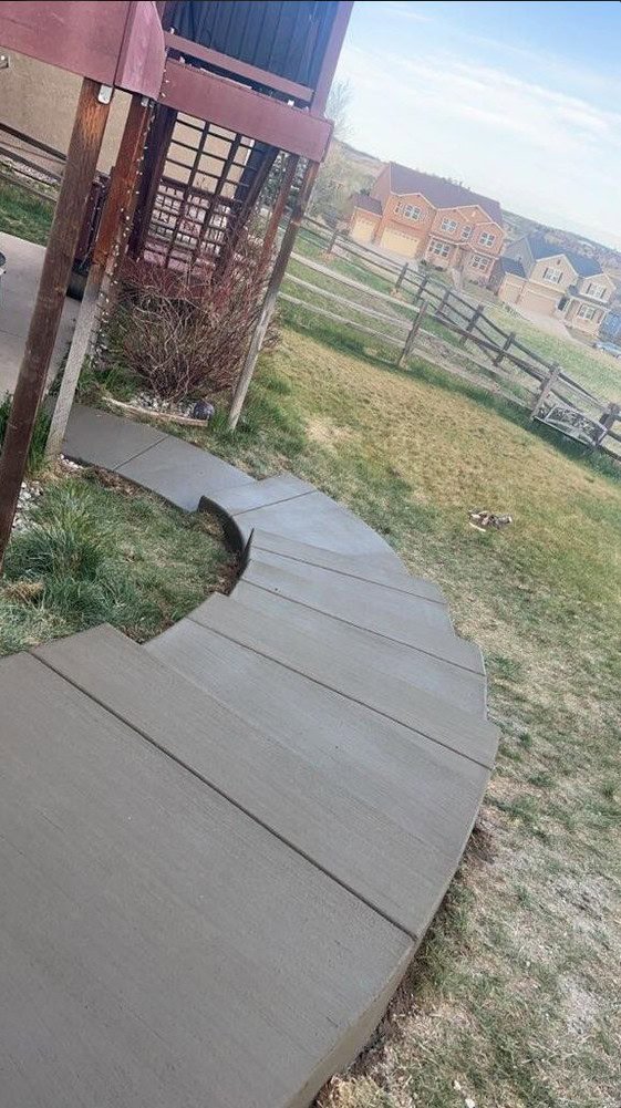 Gently curving broom‑finish concrete walkway flowing through a sloped backyard in Colorado Springs