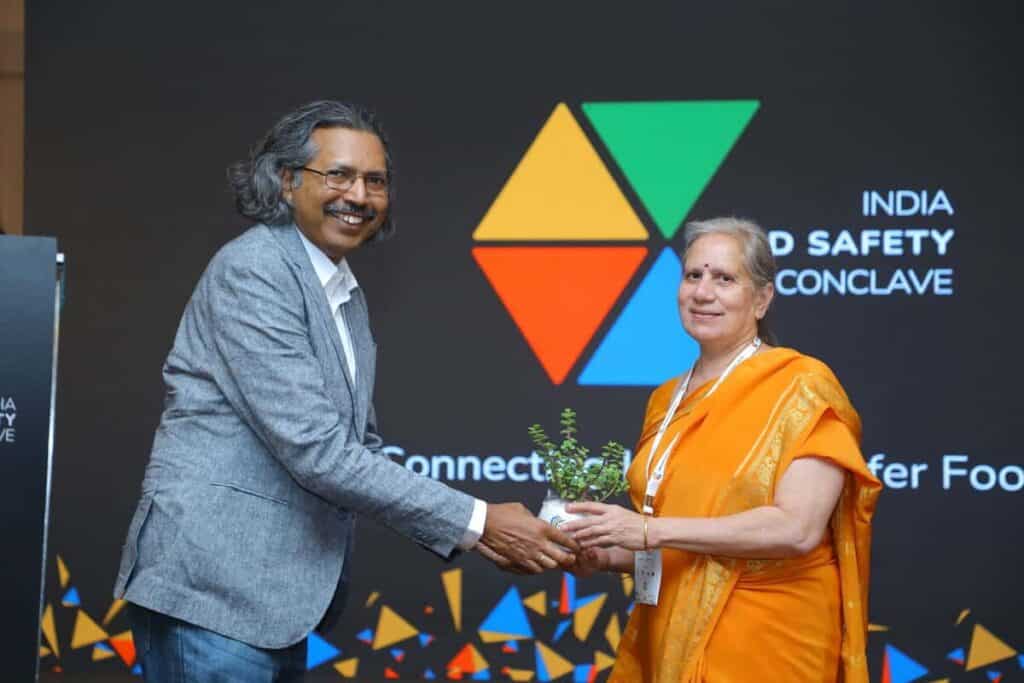 Two professionals exchanging a plant at India Food Safety Conclave 2023.