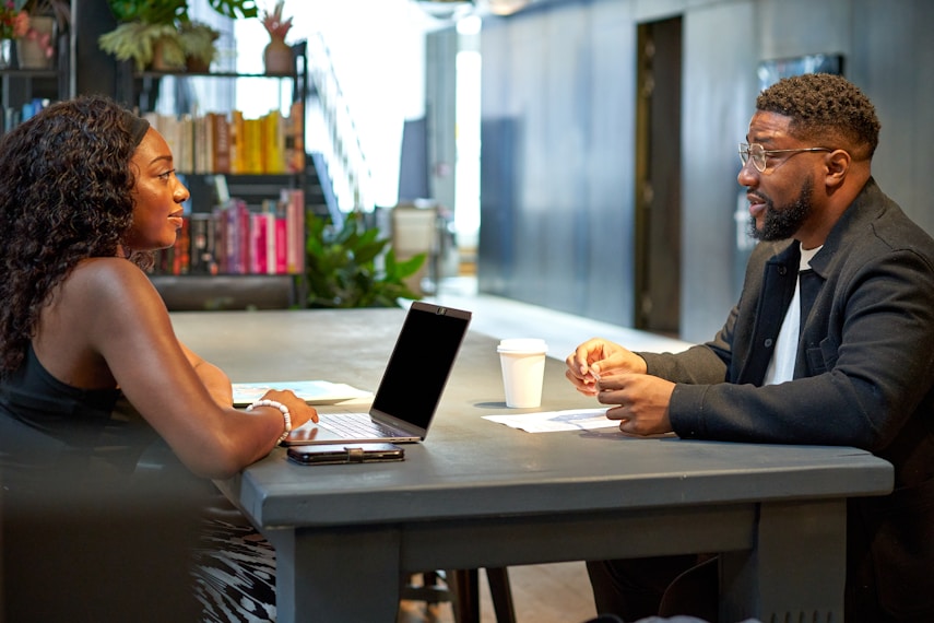 Two colleagues talking across a desk with a laptop