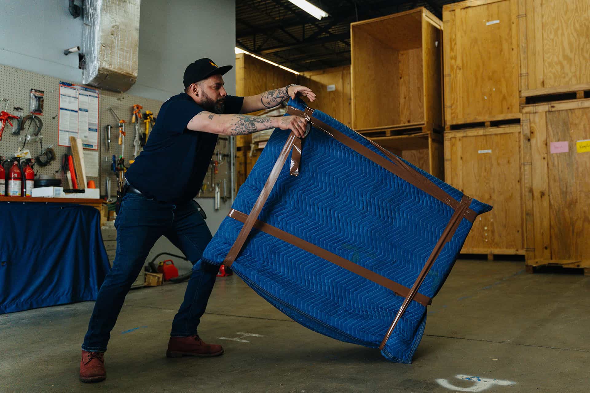 Mover handling a large blue moving blanket in a warehouse setting for Coutu Bros. Moving & Storage.
