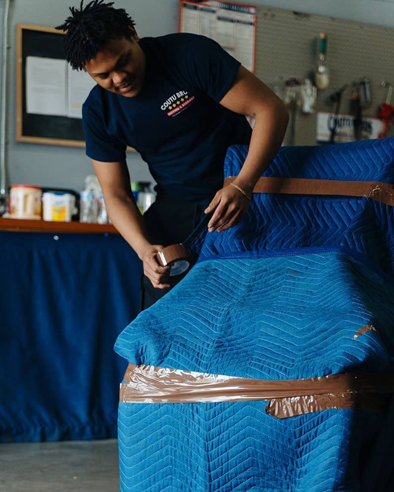 Coutu Bros. Moving & Storage employee wrapping furniture with blue moving blankets for protection.