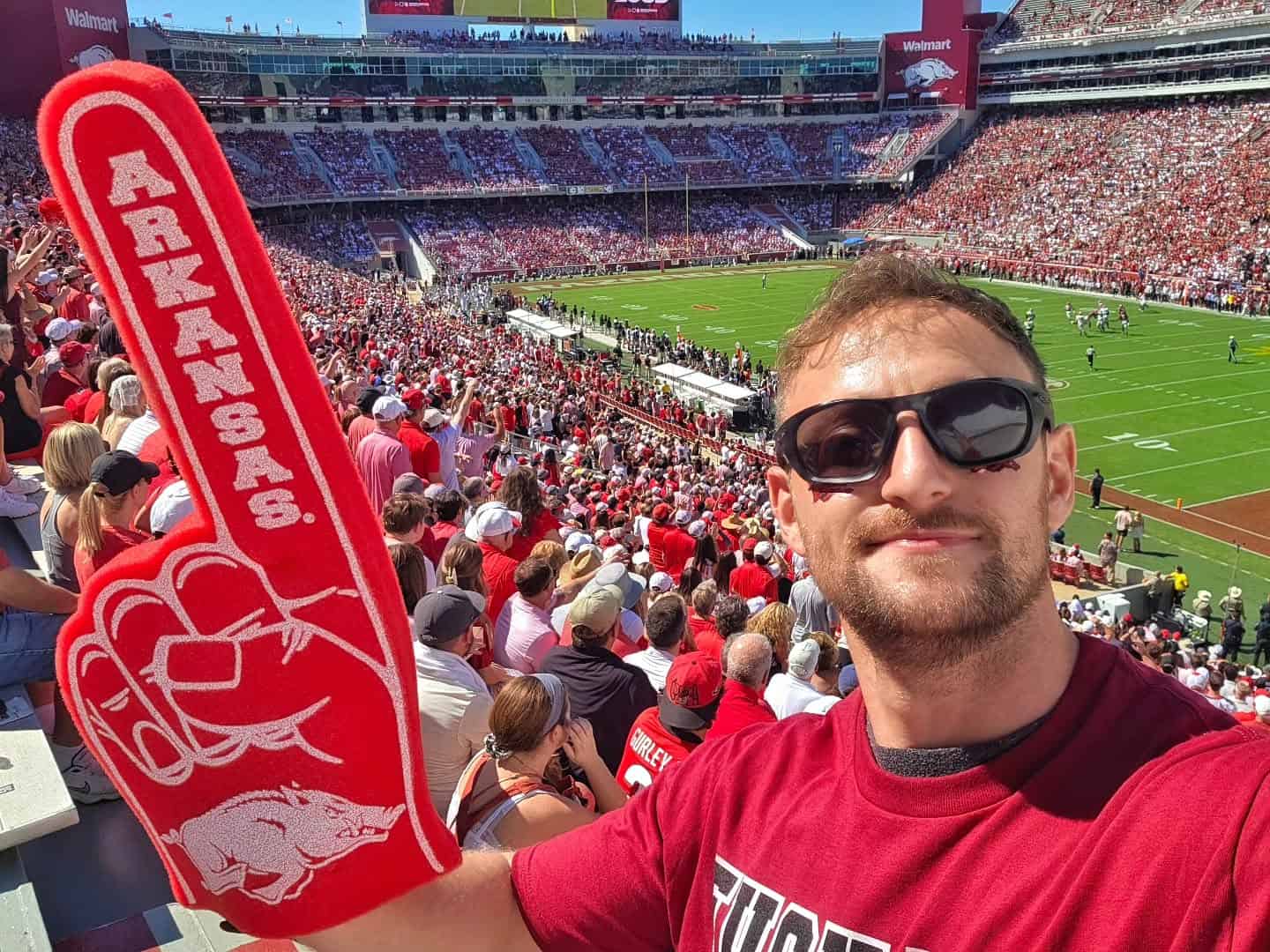 Fan holding a red Arkansas foam finger in a crowded football stadium.