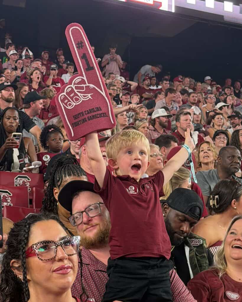 Young fan raising a garnet South Carolina number-one foam finger in the stands.