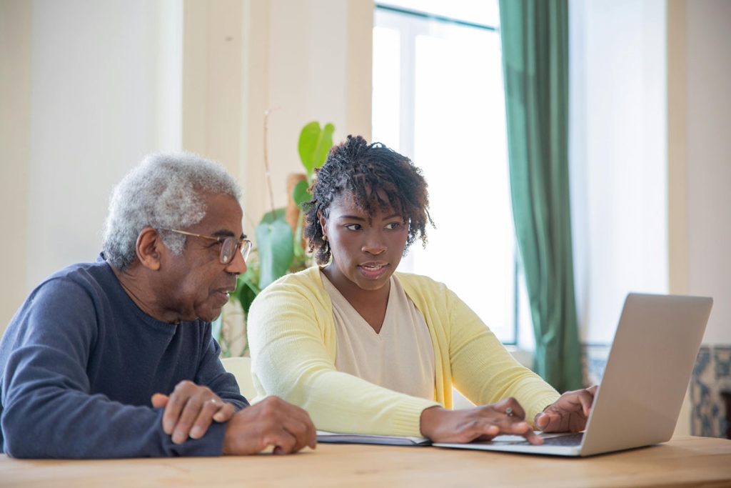 A person showing something on a laptop to an elderly man. Or, for a bit more clarity: A person demonstrating something on a laptop to an elderly man. - MEDICAID PLANNING BY NON-ATTORNEY IS A CRIMINAL ACT