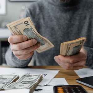A person counting stacks of ten-dollar bills, symbolizing financial management, budgeting, and planning for long-term care costs or Medicaid eligibility.