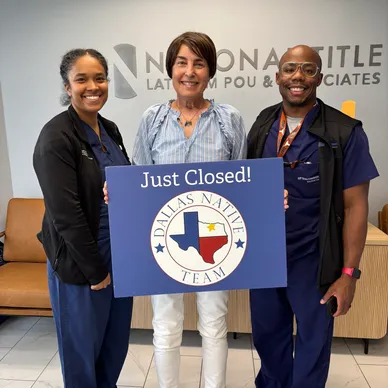 Real estate agents holding 'Just Closed' sign in North Texas office.