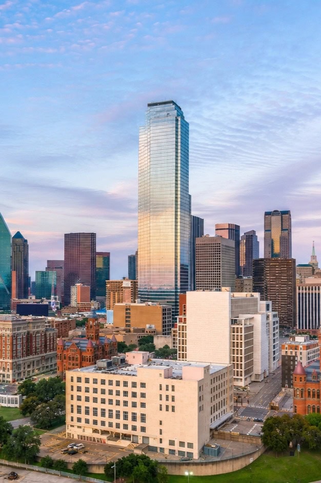 Dallas skyline featuring a tall glass skyscraper and surrounding buildings at sunset.