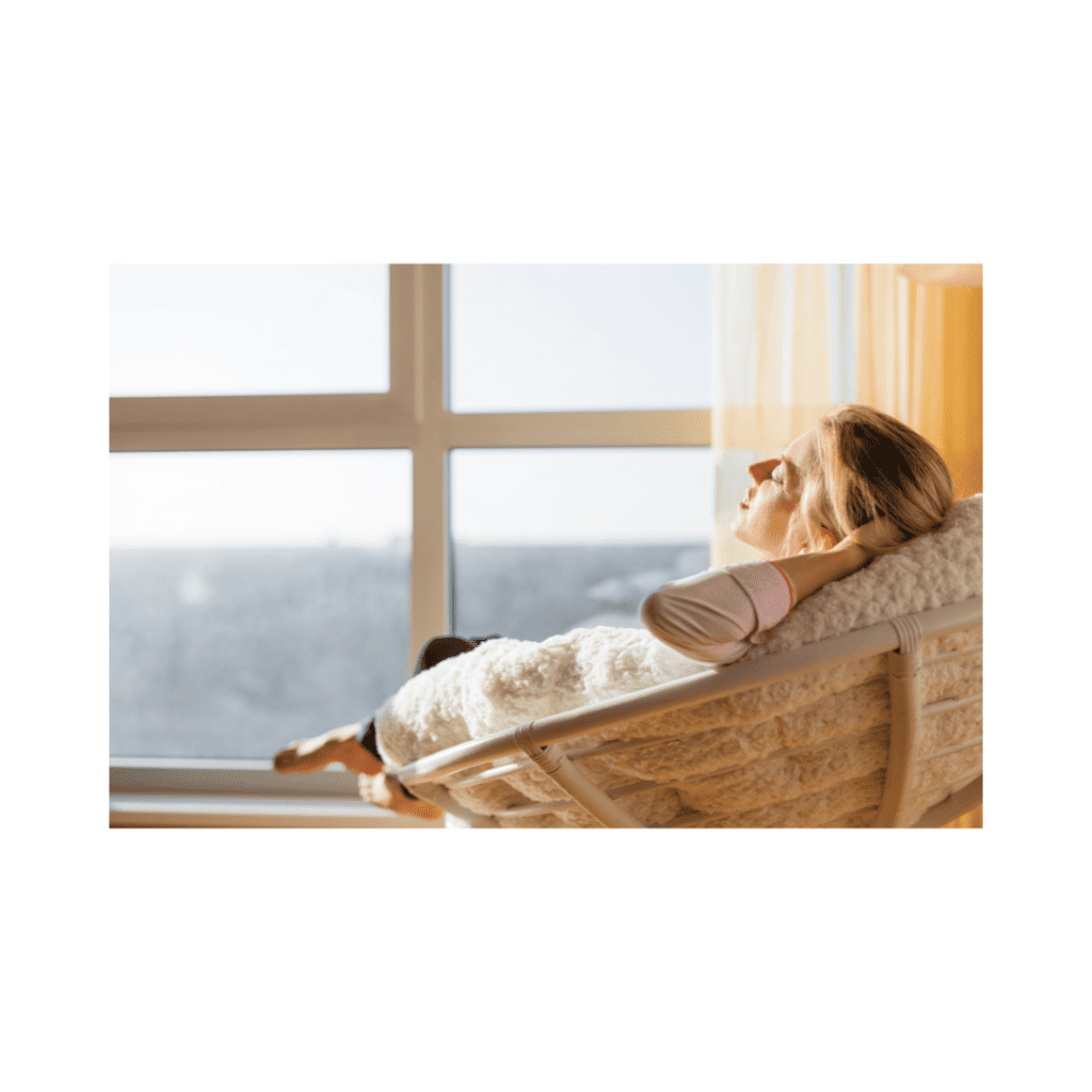 Woman relaxing with her eyes closed in a cosy chair by a sunlit window, calm and at ease