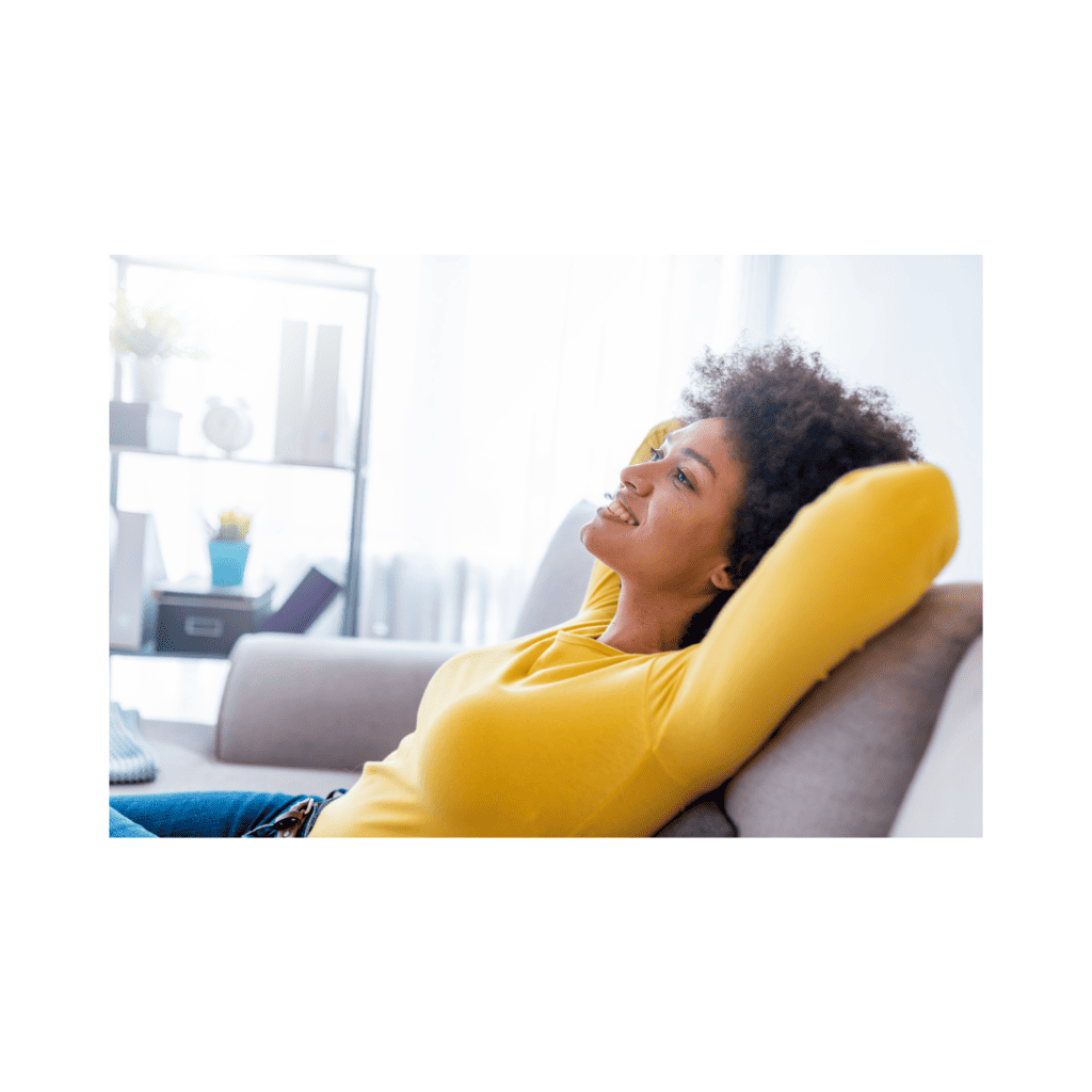A smiling woman in a yellow sweater reclining on a couch, looking calm and stress-free.