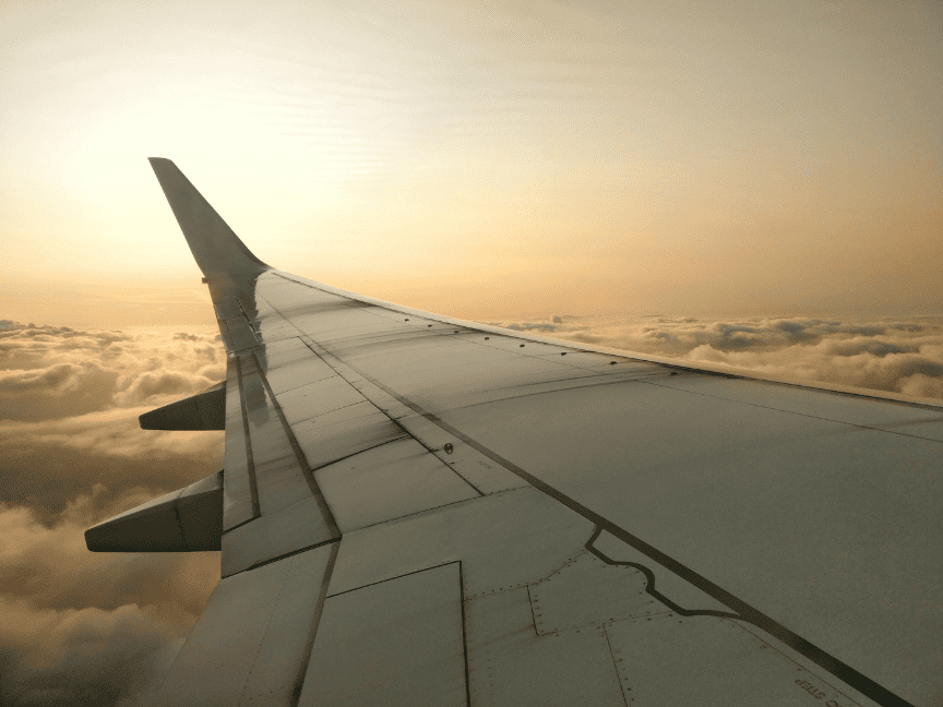 View from an aeroplane window of the wing above the clouds at sunset