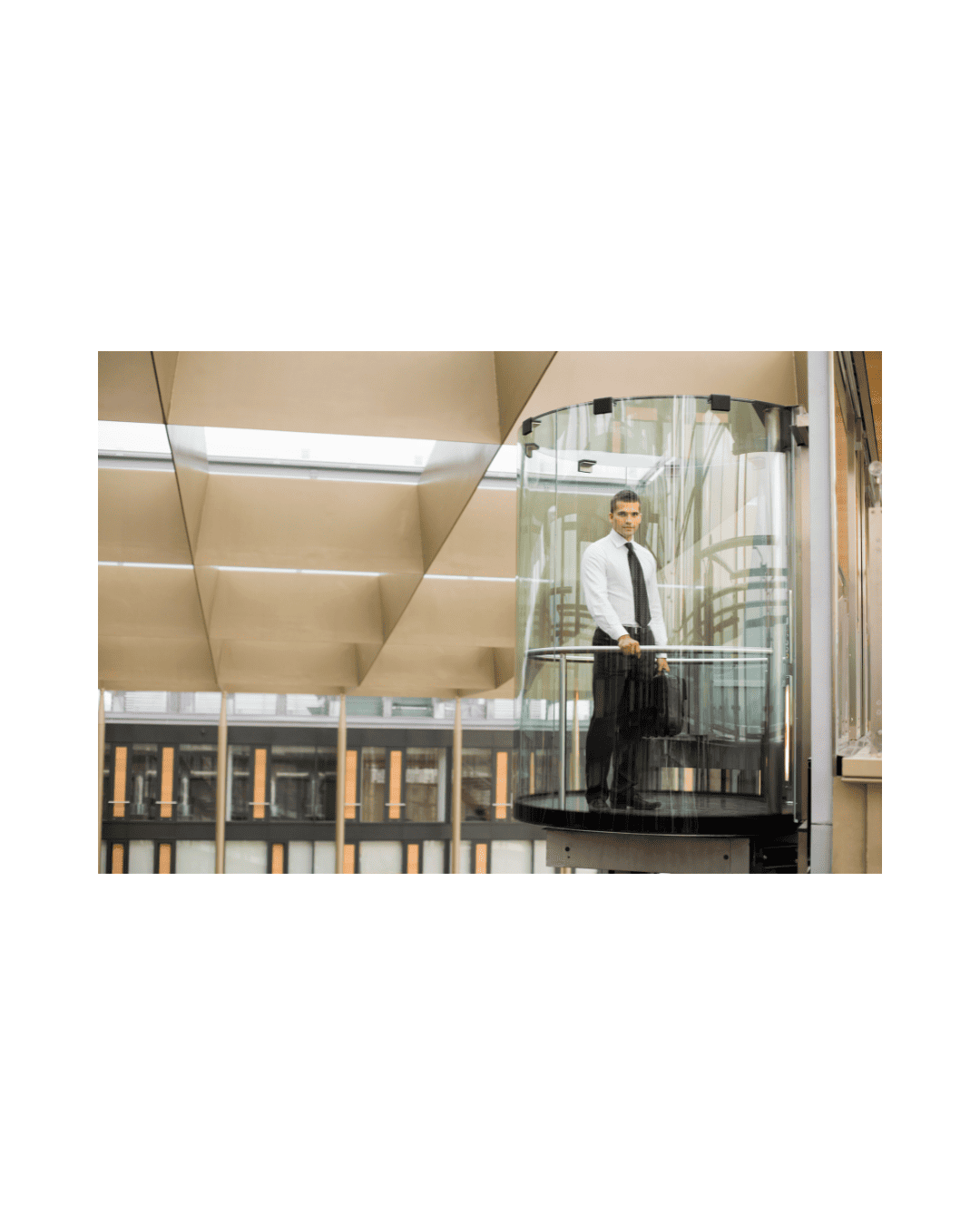 Man standing in a glass lift inside a bright building