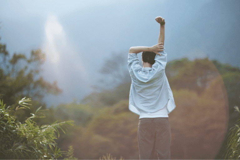 Person stretching arms toward sunlight in nature, symbolising freedom and recovery.