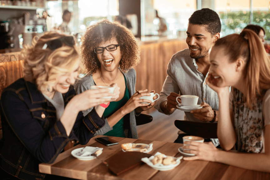 Group of smiling friends chatting together around a café table