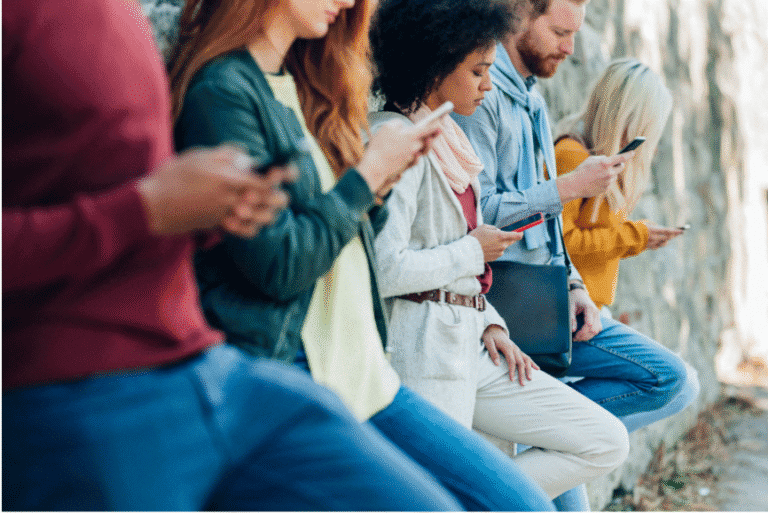Group of young adults standing in a line, each focused on their smartphone