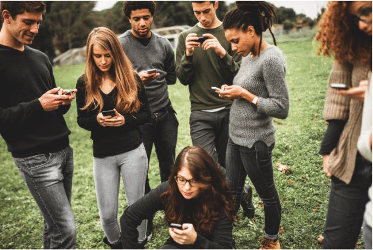Group of young adults in a park all looking down at their smartphones