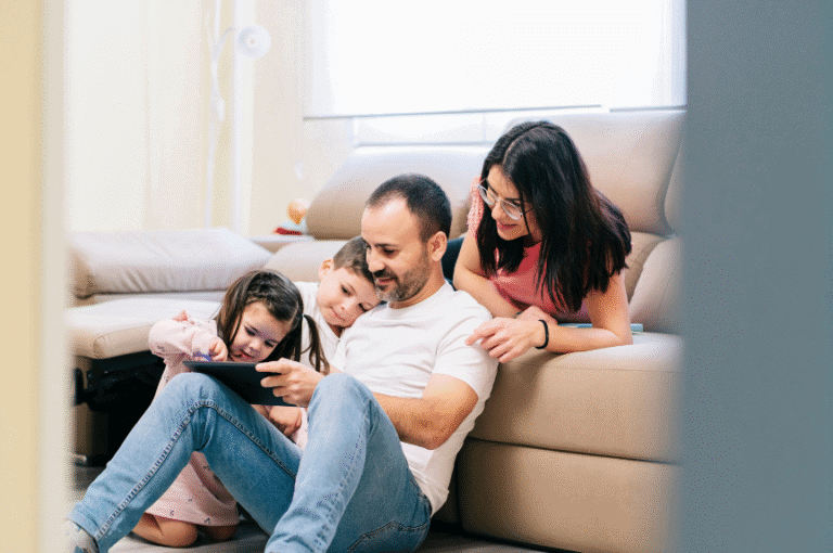 Happy family sitting on the floor using a tablet, symbolising life after recovery and reconnection.