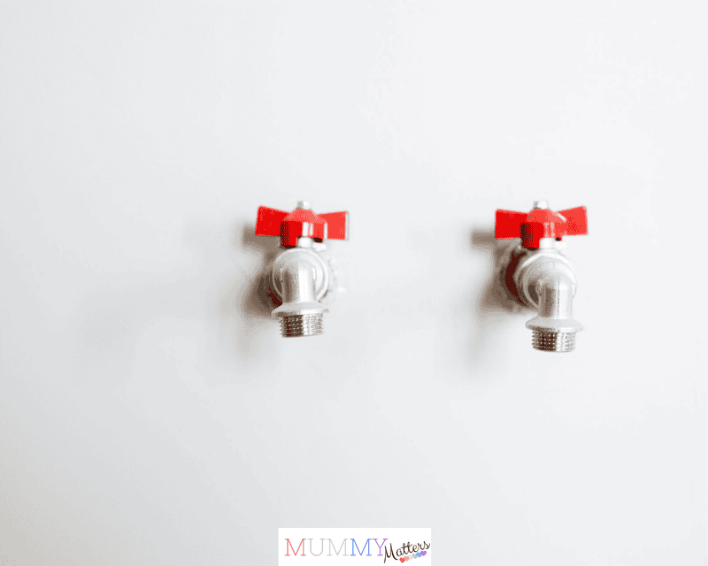Close-up of two metal faucets with red handles against a white wall, showcasing plumbing detail.
