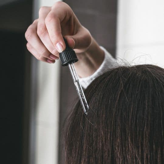 a person holding a dropper over a woman's hair