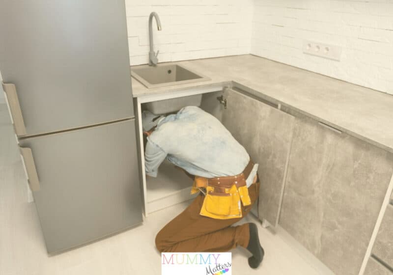 Plumber investigating a blocked drain beneath a kitchen sink
