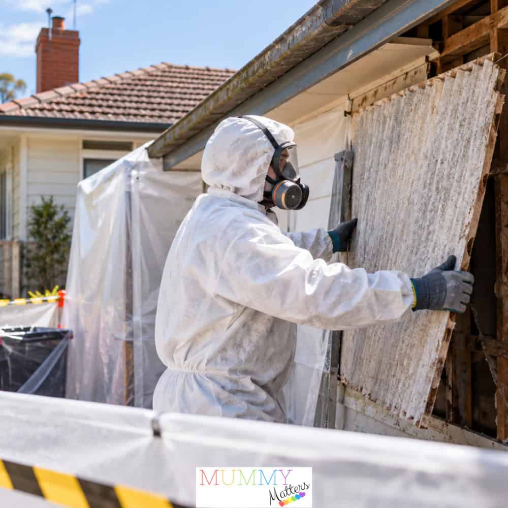 Professional asbestos removal worker wearing protective clothing and a respirator while removing old fibro sheeting from an Australian home.