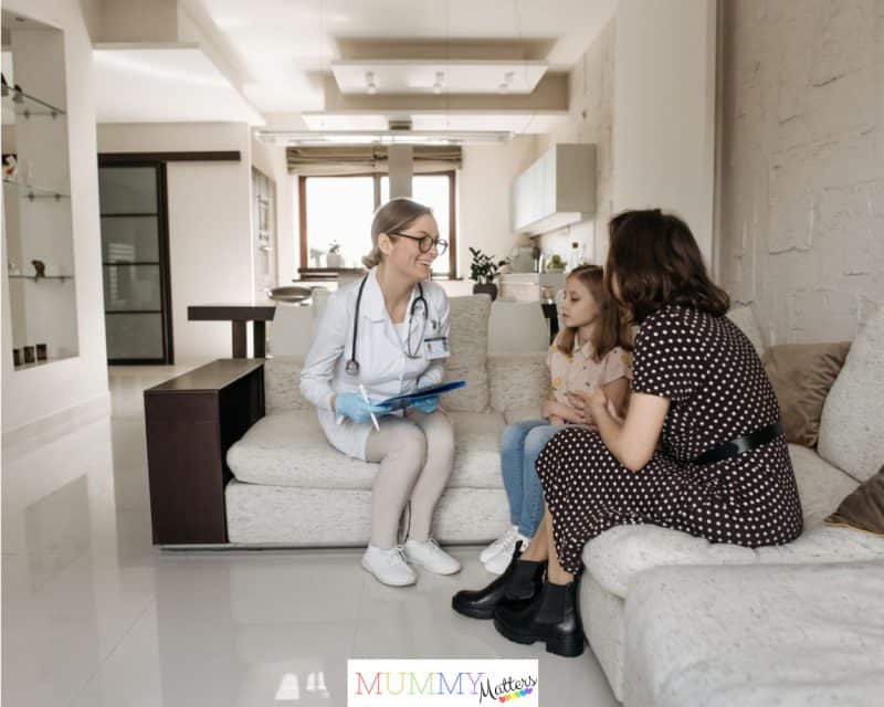 A mother and daughter receive a consultation from a female doctor at home.