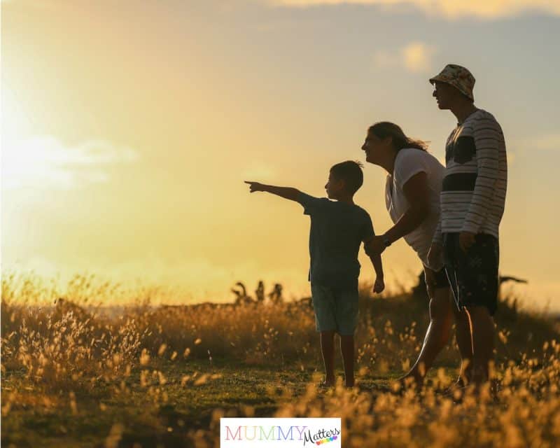 man and woman holding hands while walking on grass field during sunset