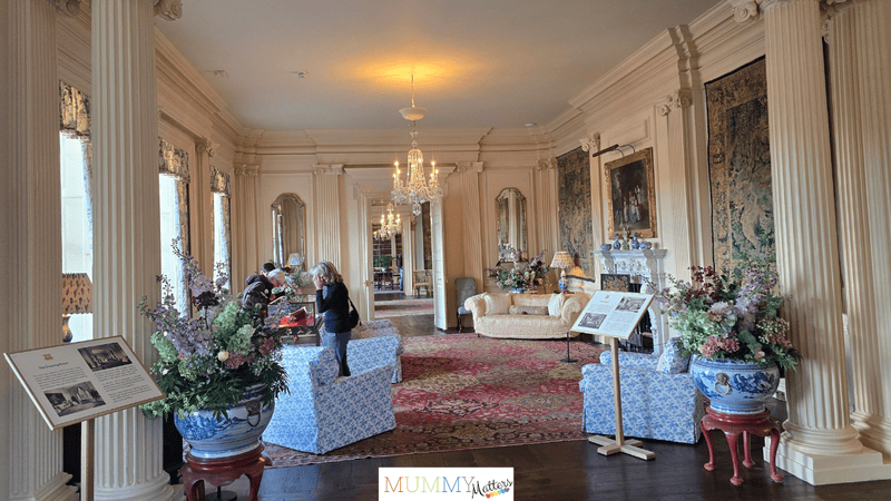 The elegant Drawing Room at Trent Park House, featuring ornate columns, chandeliers, antique furnishings and floral displays.