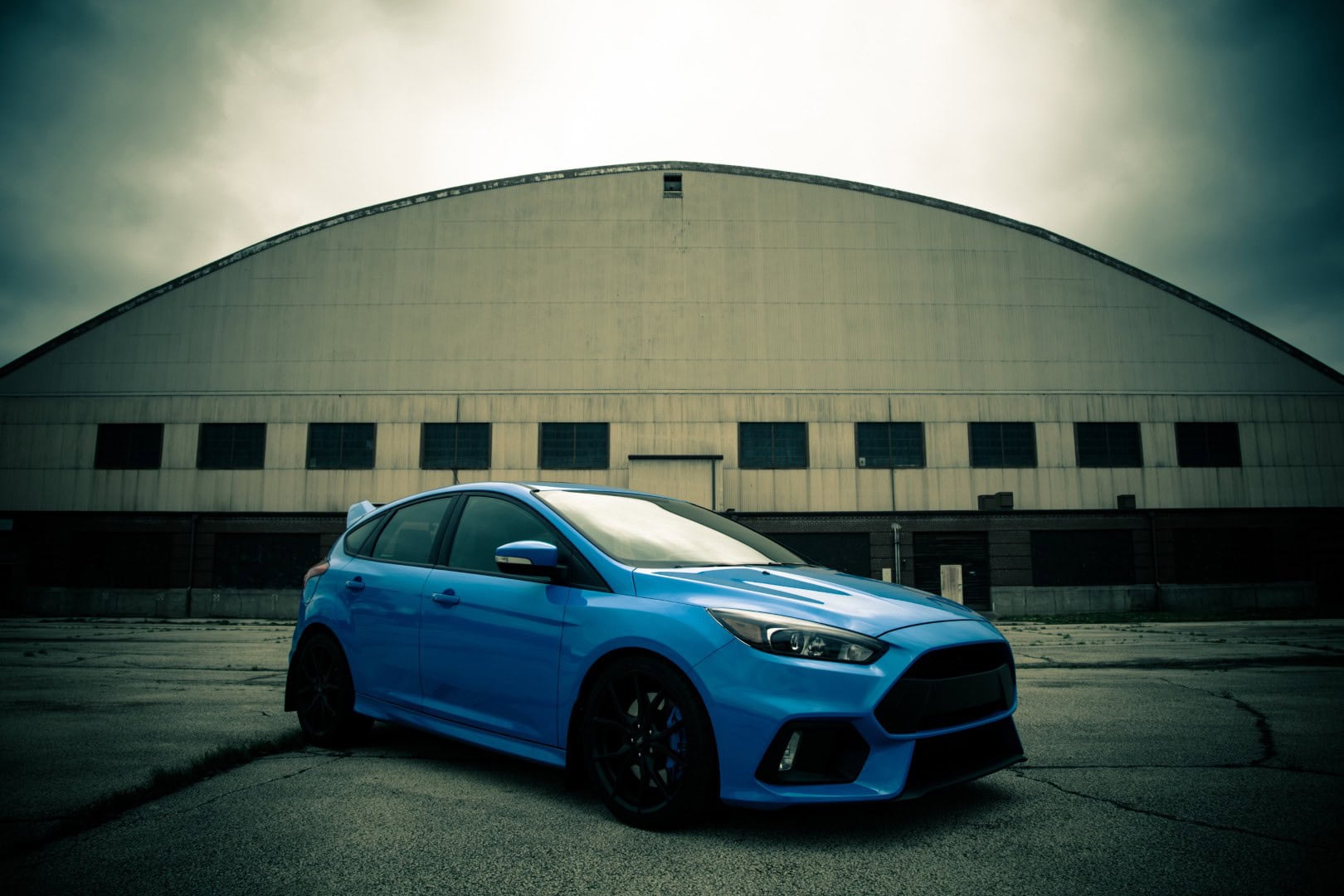 A sleek blue car parked outdoors near a large industrial building, highlighting vehicle maintenance and repair services at Del Mar Car Care.