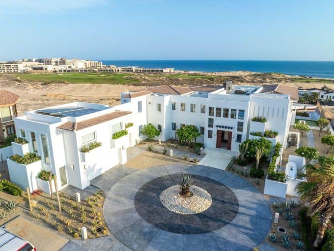 A Large White House With A Circular Driveway And A Large Building With A Beach In The Background