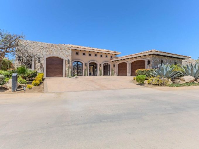 Luxury Villa With Stone And Stucco Exterior, Desert Landscaping, And Three Garage Doors At Diamante Cabo San Lucas Real Estate.
