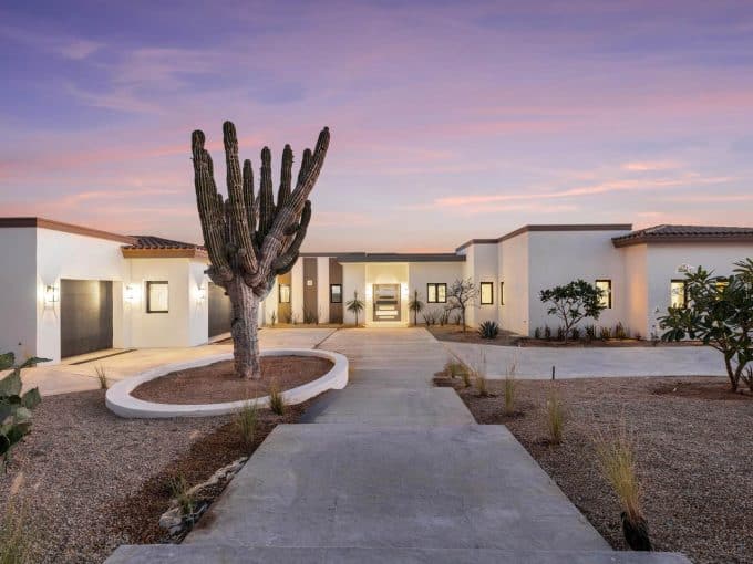 Modern Desert-Style Home In Cabo San Lucas With Minimalist Architecture, A Large Cactus In The Front Yard, And A Stunning Sunset Sky. Diamante Properties Offer Luxurious Living In Baja California.
