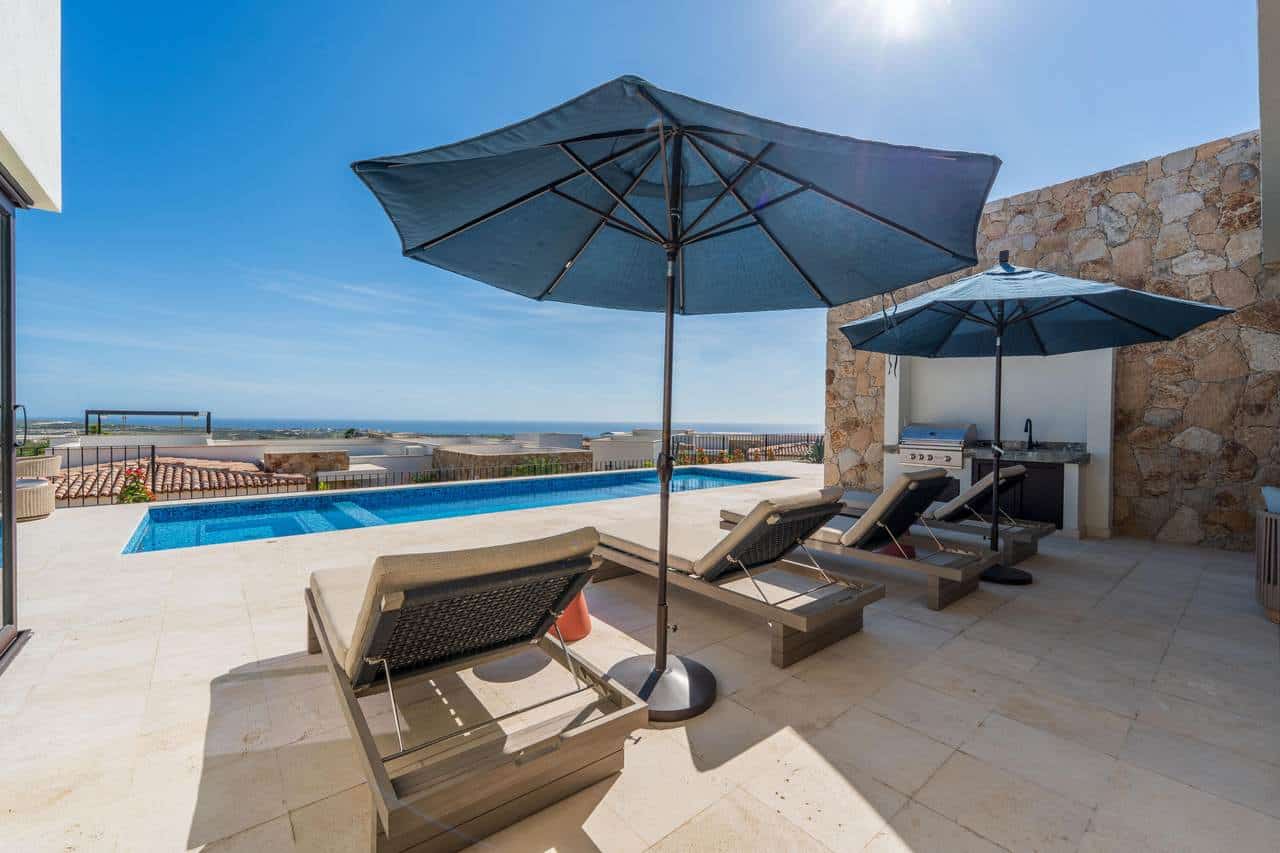 Elegant Outdoor Pool Area At Diamante Cabo San Lucas With Lounge Chairs And Shaded Umbrellas, Offering Stunning Ocean Views And Perfect For Relaxing In Luxury.