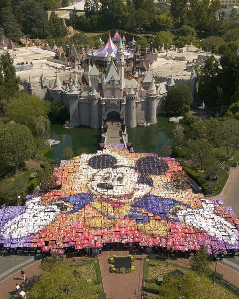 Fans gather in front of Sleeping Beauty Castle to create a Mickey Mouse mosaic, capturing Disneyland magic in iconic photos.