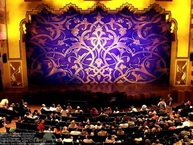 Guests eagerly await Disney’s Aladdin musical at the theater, framed by golden arches and a grand purple stage curtain.