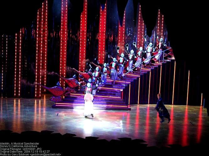 Genie and Aladdin dazzle guests at a Disney park show, joined by dancers on a glowing staircase in an Aladdin-themed performance.