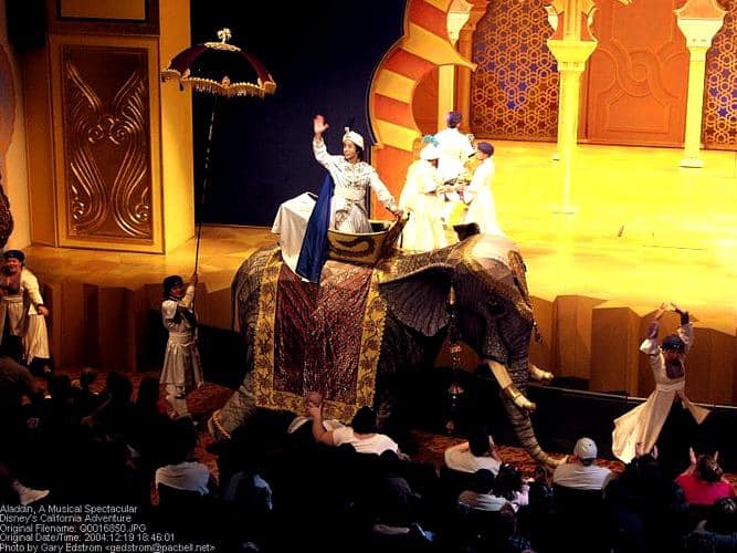 Aladdin and friends in dazzling royal costumes ride a giant elephant prop on stage, enchanting the audience at Disney’s Broadway show.