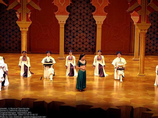 Jasmine dazzles center stage in her green costume, joined by dancers in white and purple, evoking a magical Aladdin show.