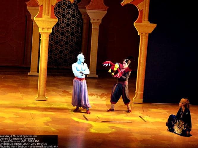 Aladdin, Jasmine, and Genie light up the stage at Disney's Aladdin musical, framed by golden arches and magical lighting.