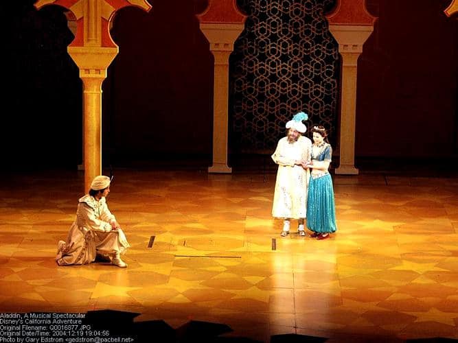 Aladdin, Jasmine, and Genie dazzle guests onstage with a golden floor and ornate set in a magical live performance.