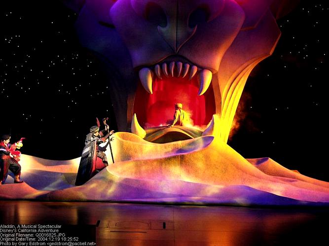 Aladdin musical stage at Disney, featuring a glowing tiger head centerpiece and performers in vibrant costumes captivating the audience.