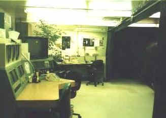 Backstage-style office with desks, chairs, computers, and papers—like an entertainment crew area—open space beyond.