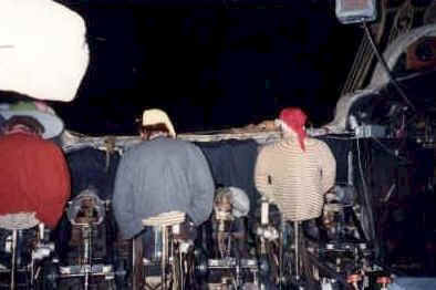 Three crew members backstage at Disney World sit at a control panel, hats and jackets on, managing the show’s behind-the-scenes magic.